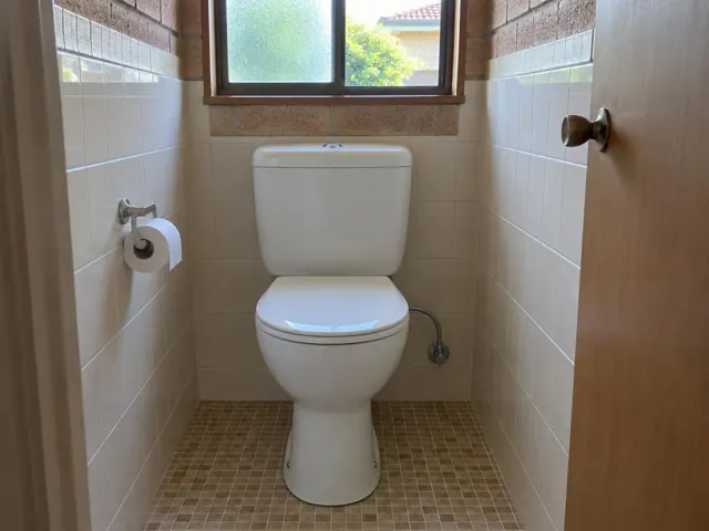 Clean white toilet in a small tiled bathroom with window and toilet roll holder in Baulkham Hills