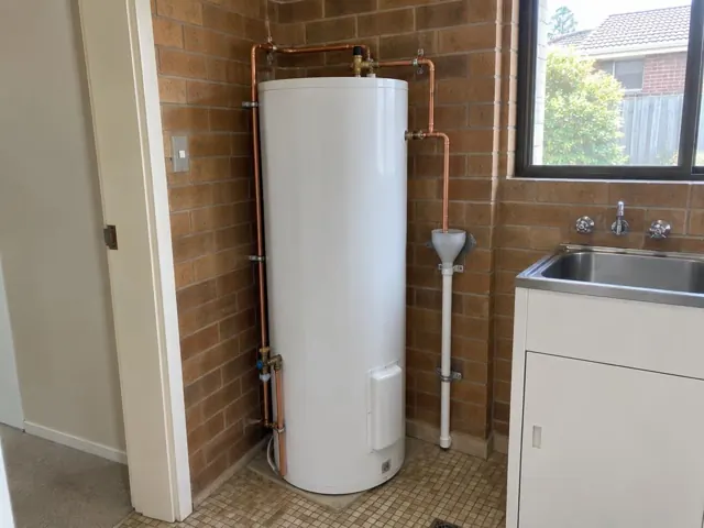 Indoor hot water cylinder with copper pipework beside a laundry sink and brick wall in Castle Hill