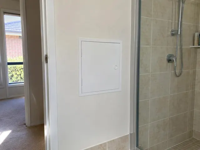 Small access panel on a painted bathroom wall beside a tiled shower in Beaumont Hills